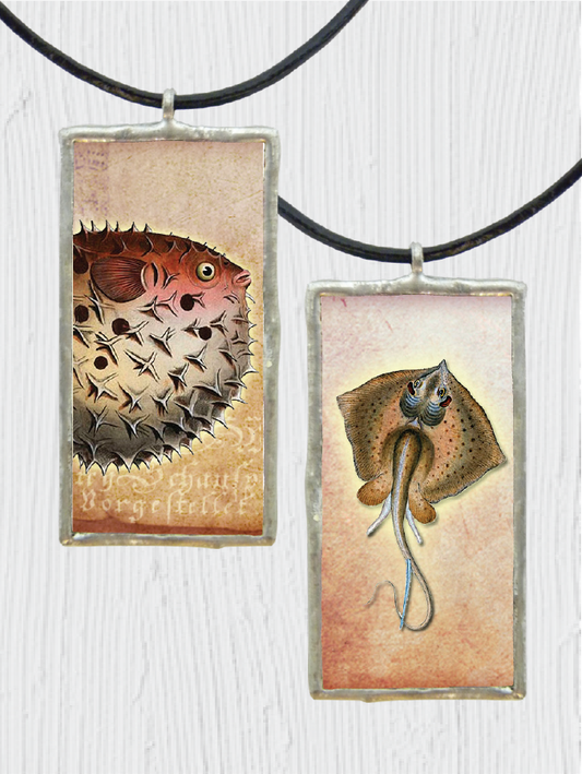 Two pendant necklaces with fish designs on a textured white background
